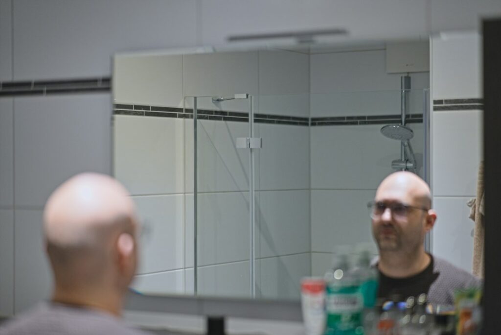 Bärtiger Mann bei der Bartpflege vor dem Badezimmerspiegel